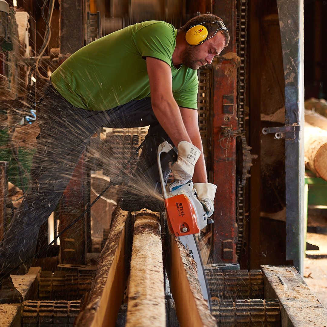 Pracovník řeže dřevo motorovou pilou ve výrobní hale